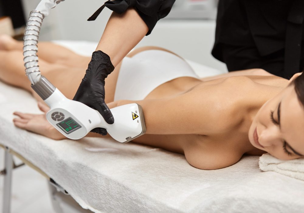 close-up of masseur arm doing endosphere theraphy on woman arm with professional device, naked girl in spa having massage for body